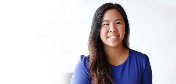 A female employee wearing a blue top, smiling at the camera in a bright office setting.